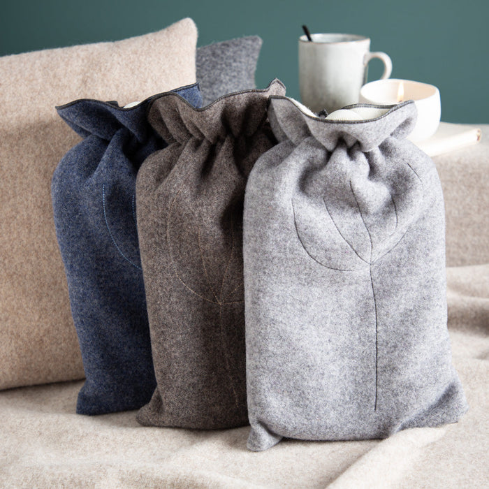 Wärmflaschen mit Bezug aus Merinowolle liegen auf einem Stapel