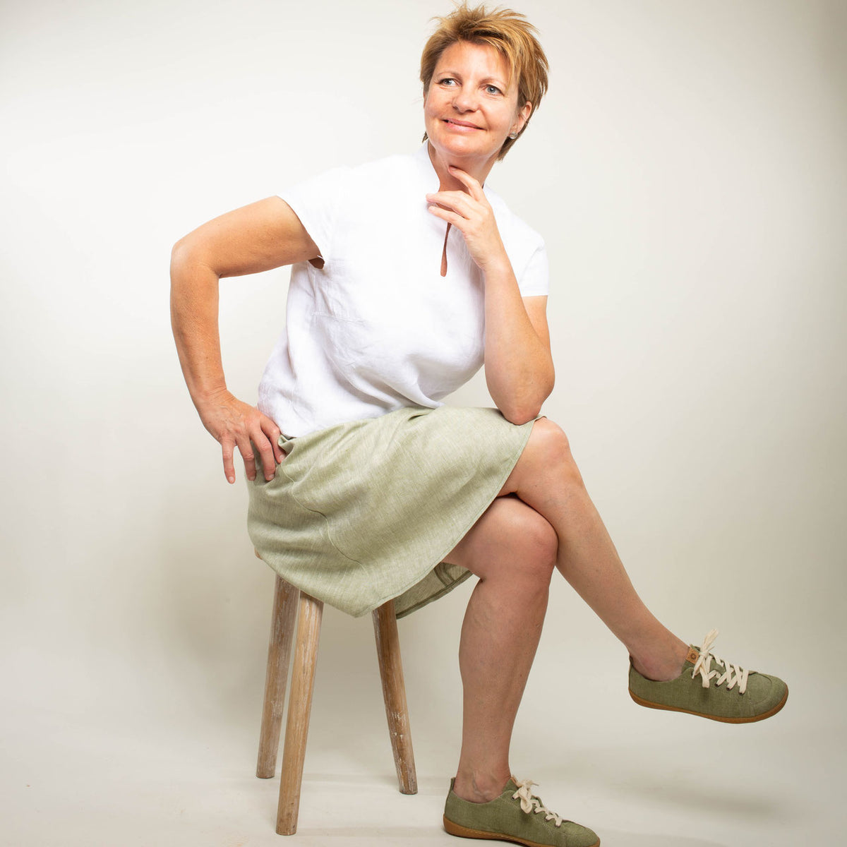 Frau mit weißer Bluse und grünem Leinenrock sitz auf einem Hocker